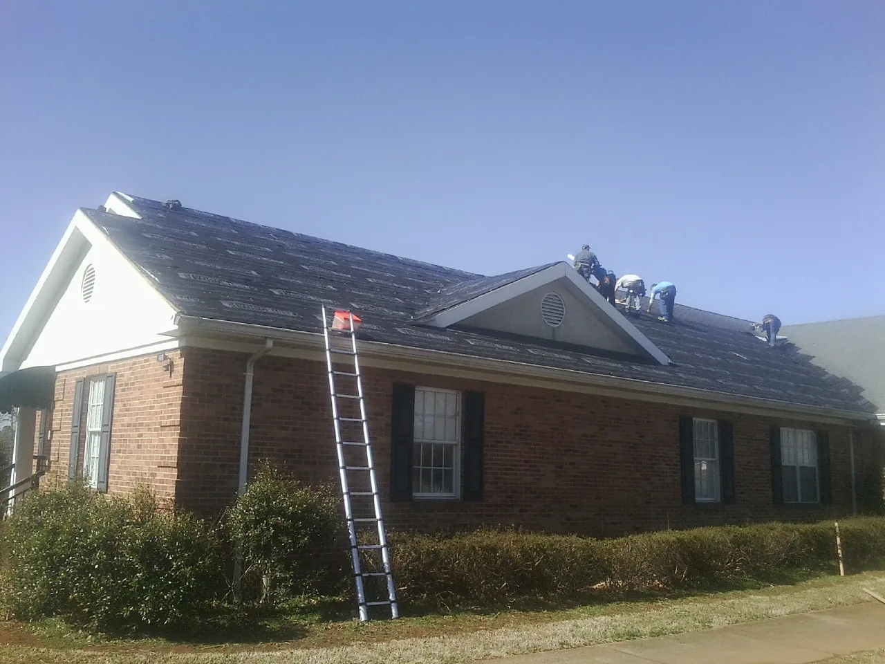 Crew tearing shingles off a brick ranch roof with a ladder set — Metal Roof Repair work by our crew in Morris